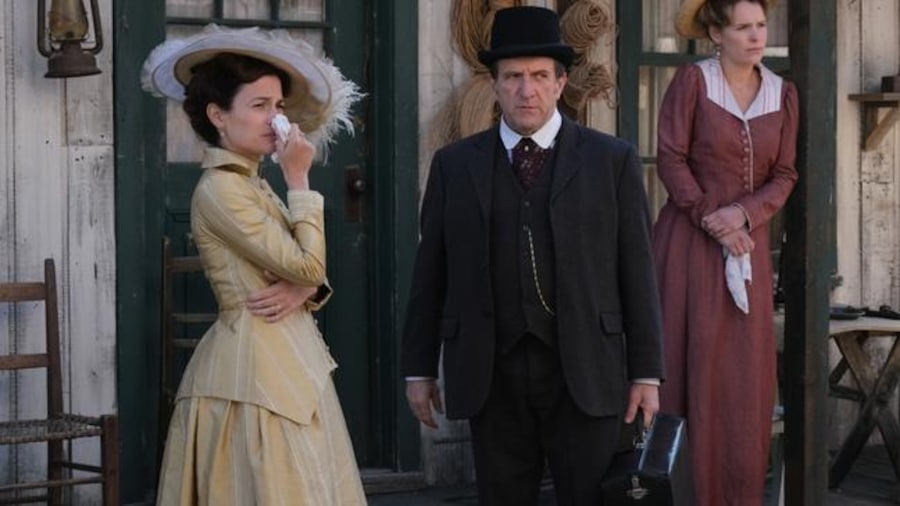 The two women and the man, in old clothes, look into the distance and appear sad.