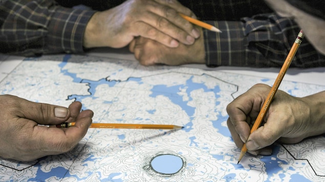 Des mains pointent avec des crayons certains endroits sur une carte géographique.