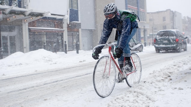 Une personne circule à vélo dans une rue enneigée de Montréal.