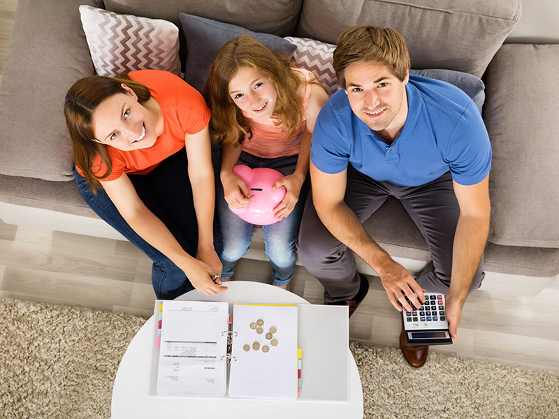 Jeune famille assise sur un sofa, dressant un budget avec une calculatrice.