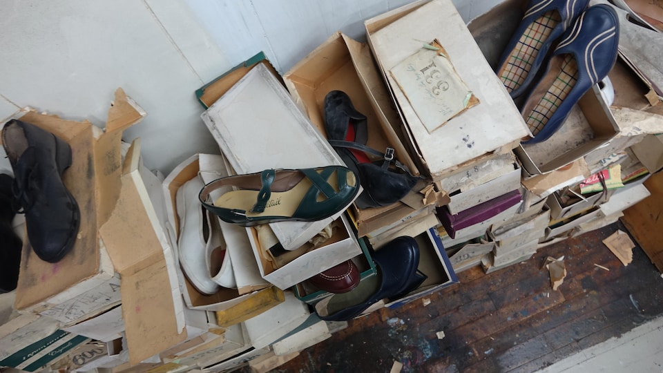 Piles of old cardboard boxes stacked on top of each other.  Inside some are women's shoes.