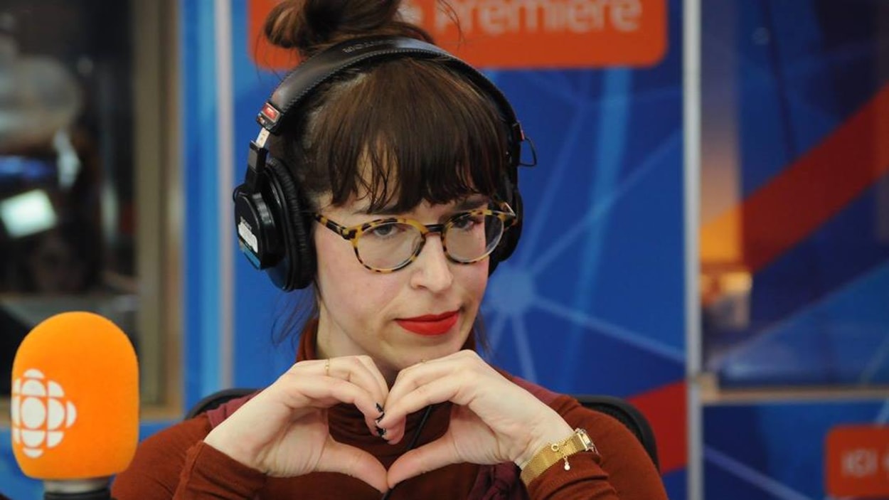 Young woman making a heart with her own hands, sitting in a radio studio.