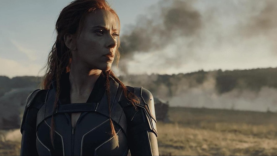 A woman in a superhero costume watches the horizon.  A plume of black smoke appears in the background.