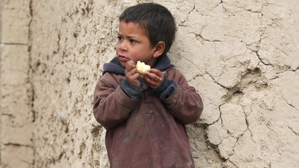 Boy eating an apple near the wall.