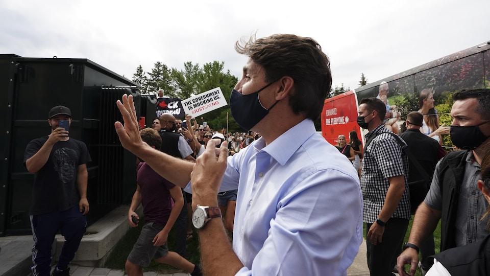 Justin Trudeau raises his hand in salute as protesters hold banners in the air.