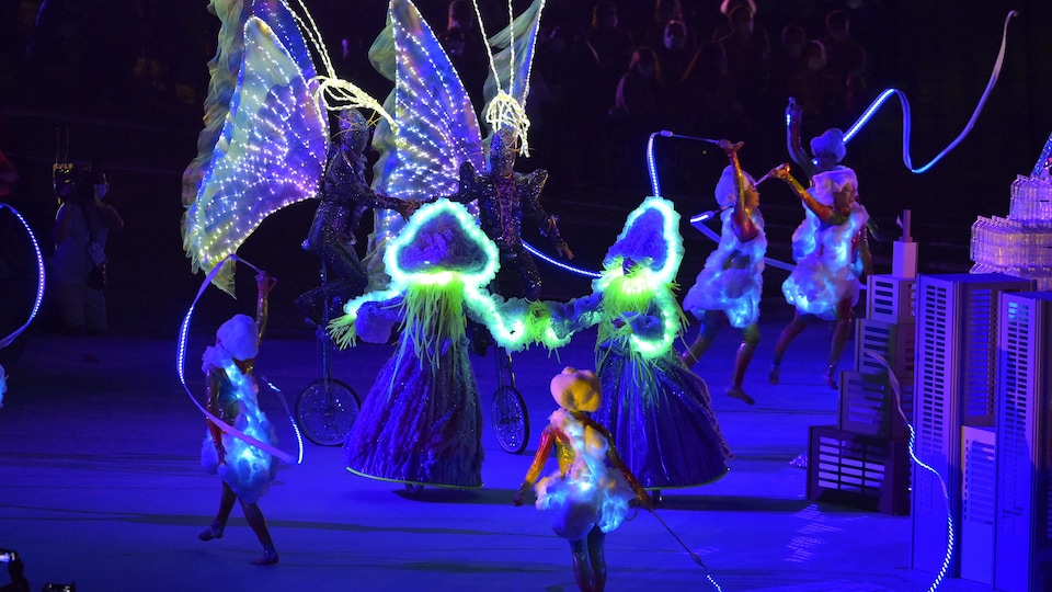 Artists dance and perform routines in luminous costumes. 