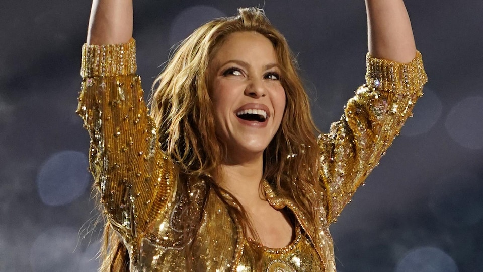 Shakira smiles and throws her arms in the air. 