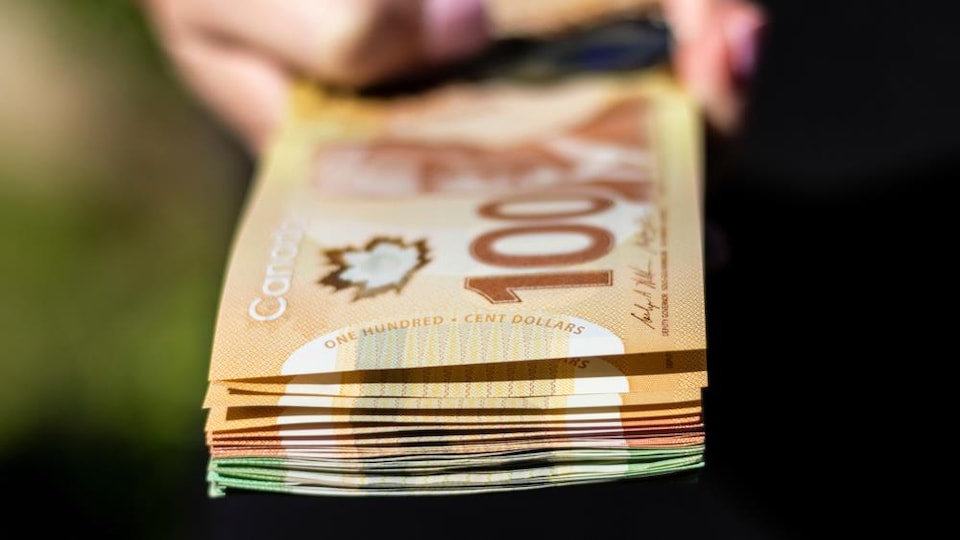 Hand holding a stack of Canadian 100, 50 and 20 dollar banknotes. 