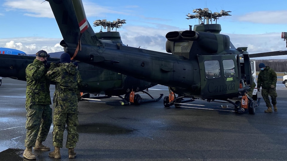 A large Canada inscription military helicopter on the tarmac with uniformed soldiers around it.