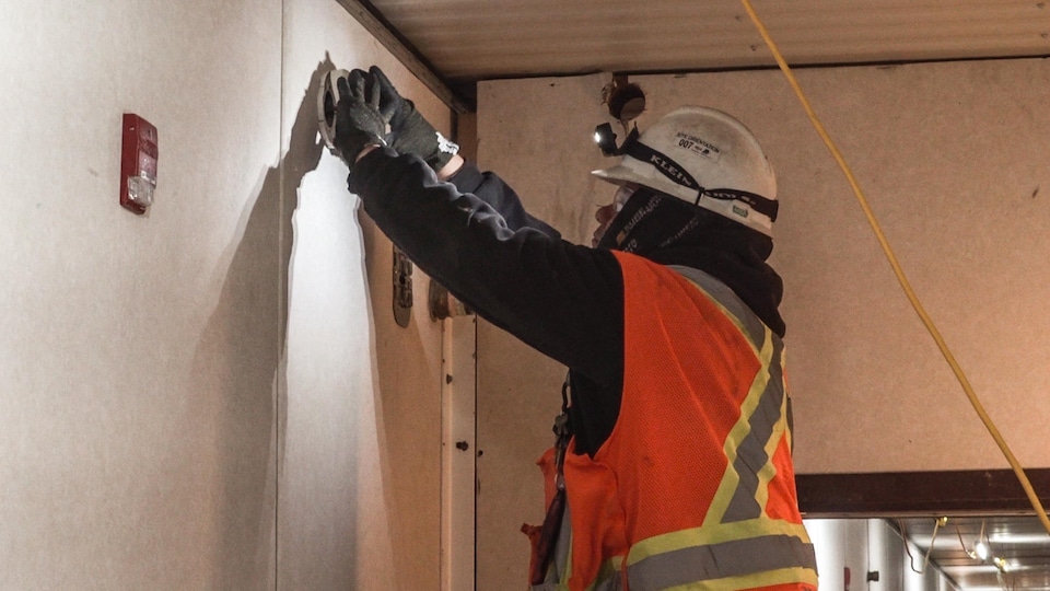 A worker on a ladder installs carbon monoxide detectors on the walls