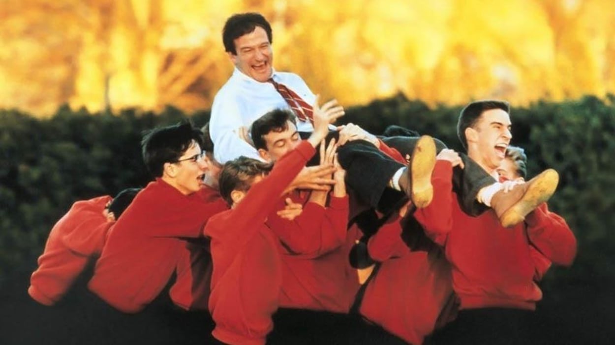 A man in a shirt and laughing, carried in victory several young men in a red jacket.