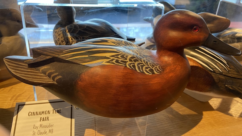 An orange carved wooden duck is displayed in a set. 