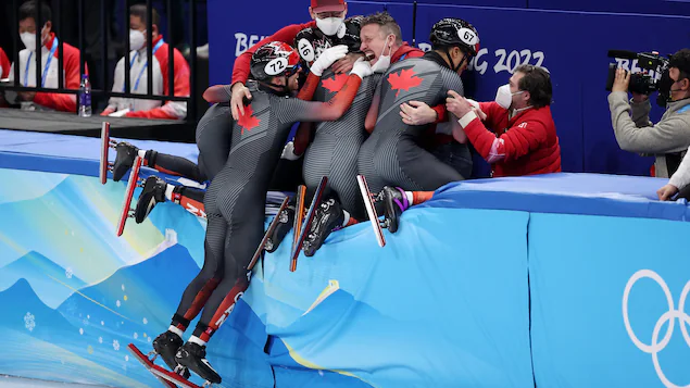 L'équipe de patinage du Canada célèbre une médaille en sautant par-dessus la bande.