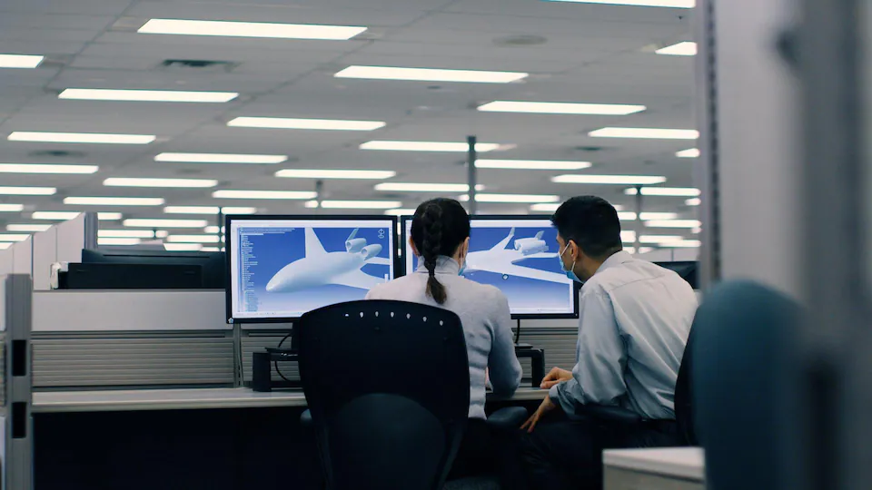 Two people sitting in front of computer screens.