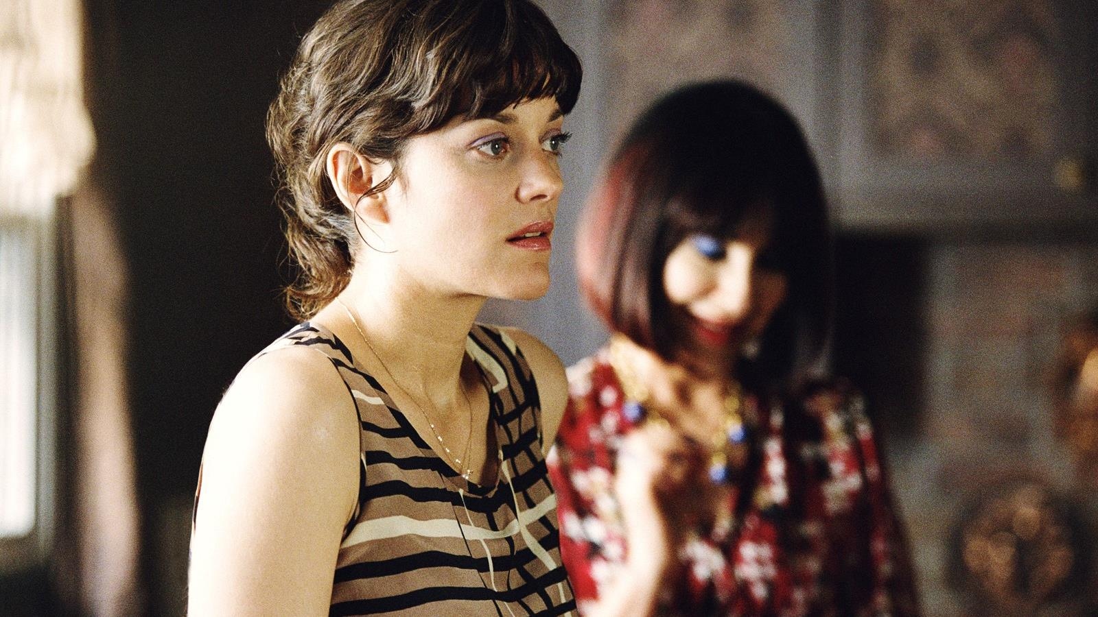 A busy-looking woman (Marion Cotillard) in front of a woman in a flashy outfit (Natalie Bay).