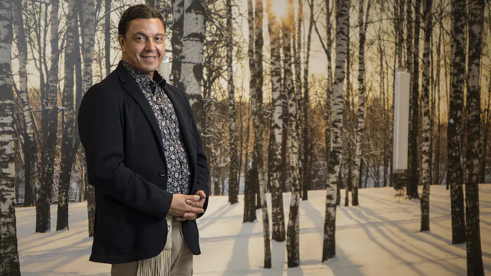 The man is standing in front of a painting representing a forest.
