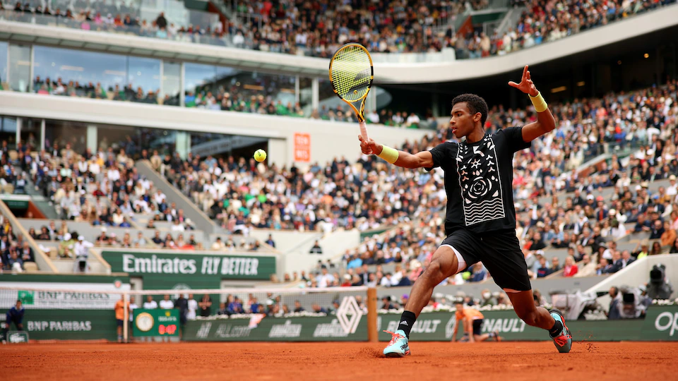 A tennis player wearing a black uniform stretches to hit a back ball during a match at Roland Garros. 