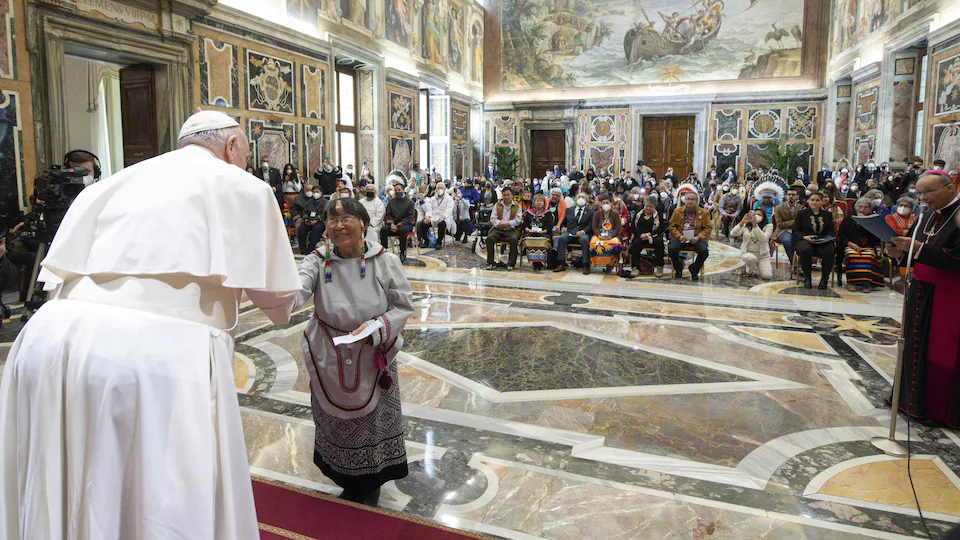 The Pope shakes hands with an Enoch woman in front of a full house