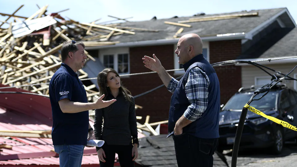 Three politicians discuss in front of the damage caused by the storm.