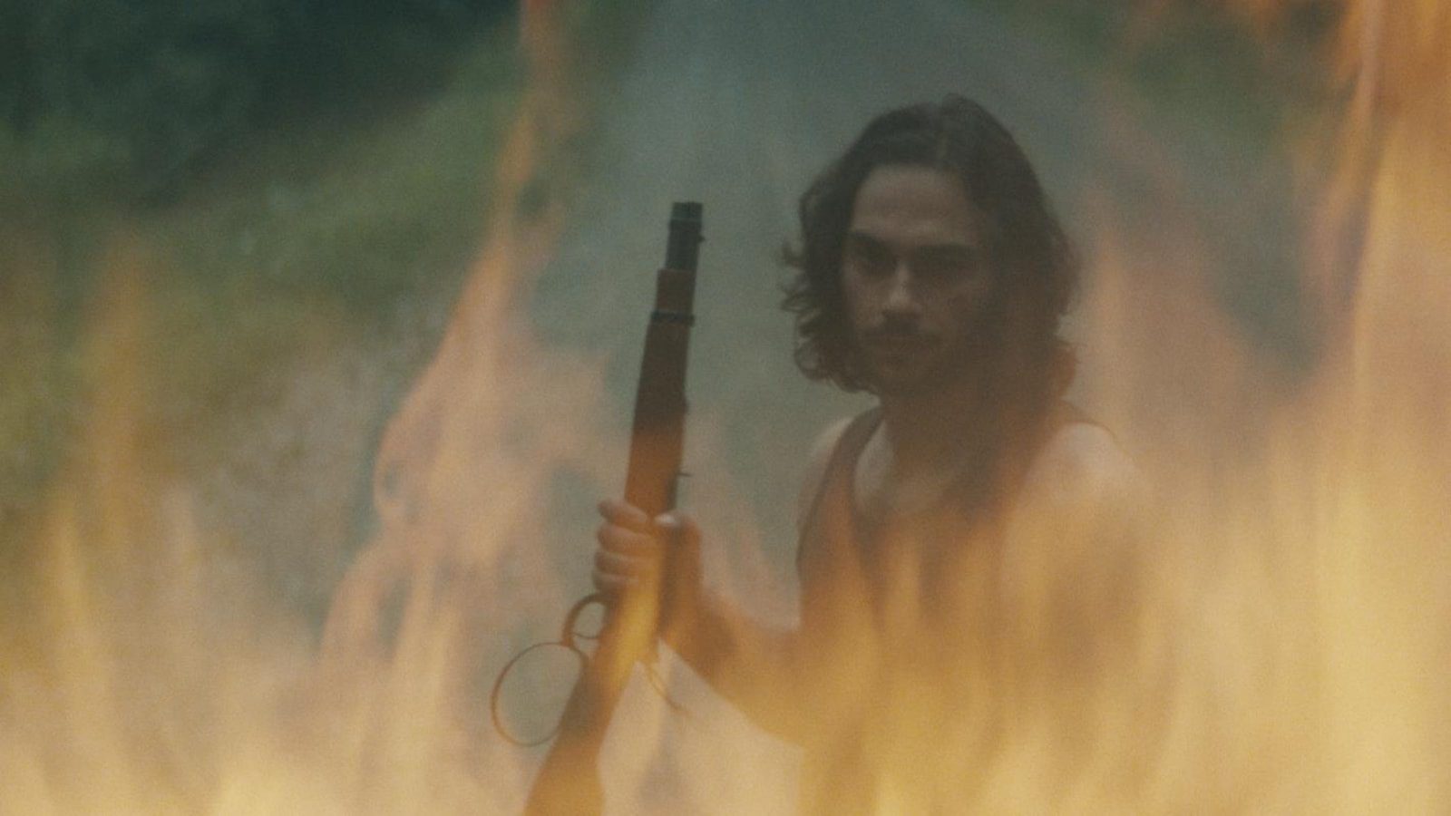 A young man with a pistol is seen through the flames.