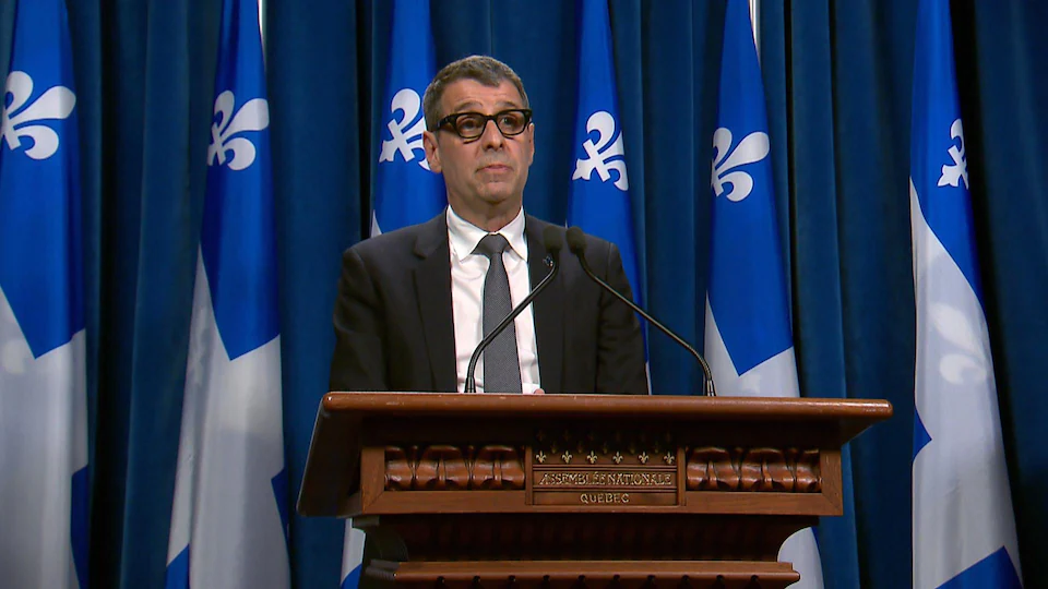 Eric Dohemy during a press conference at the National Assembly.  Standing behind a pulpit and in front of Quebec flags.