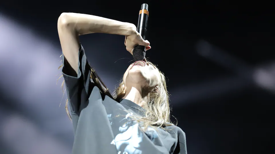 The singer raises her head back and holds her microphone in front of her mouth. 