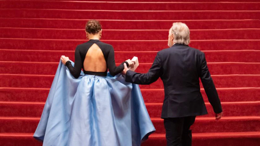 From behind, a woman in an evening dress and a man in a suit climb the red steps.