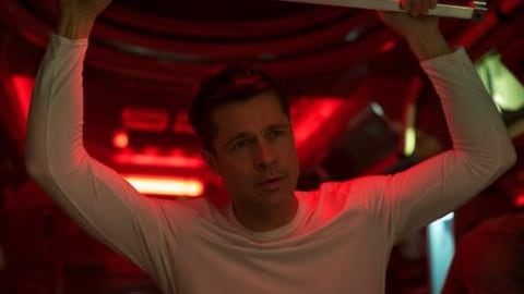 A man (Brad Pitt) in a white shirt with arms up in a red room.
