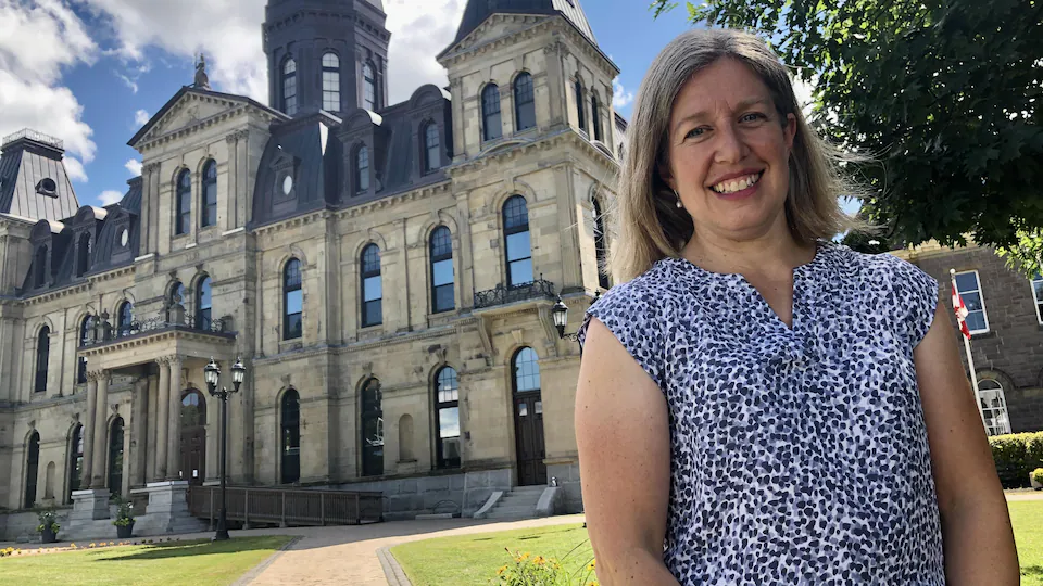 Portrait of Susan Holt smiling in front of the New Brunswick Legislative Assembly. 