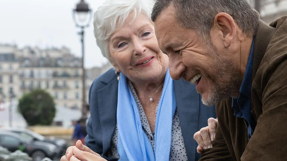 An elderly woman and father share a conspiratorial moment on the streets of Paris.