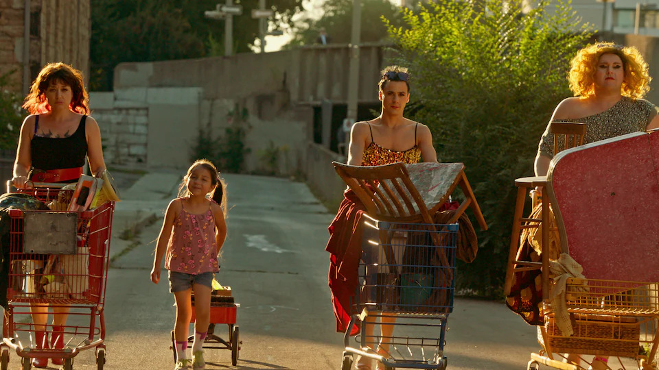 Picture from the movie.  In an alley, three adults push a grocery cart full of chairs, cloths, and other things, while a little girl pulls a cart.